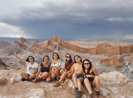 Group of 6 friends sitting on the ground, in the background is the Cordillera de la Sal.